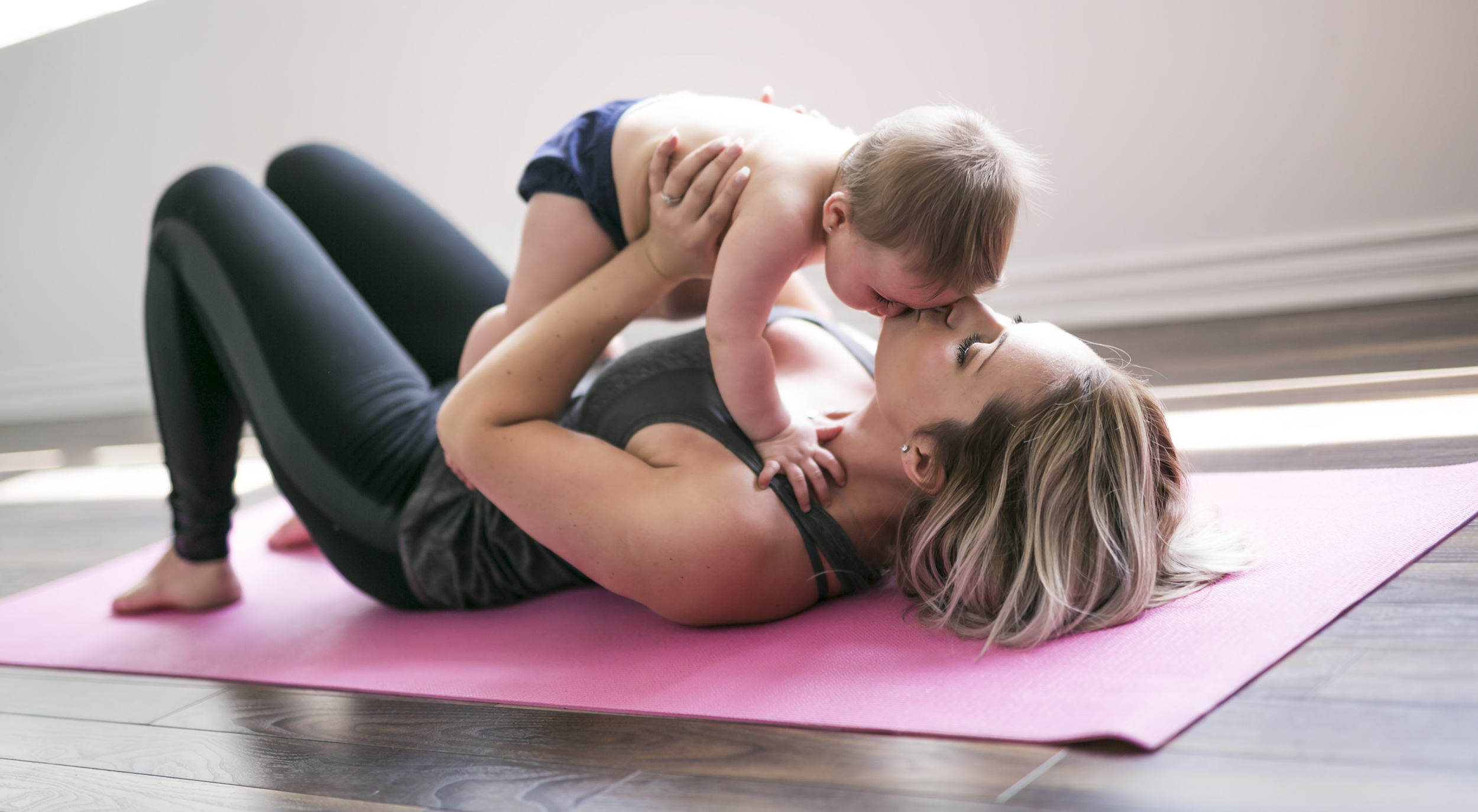 A young mother does physical yoga exercises together with her baby after a mommy makeover